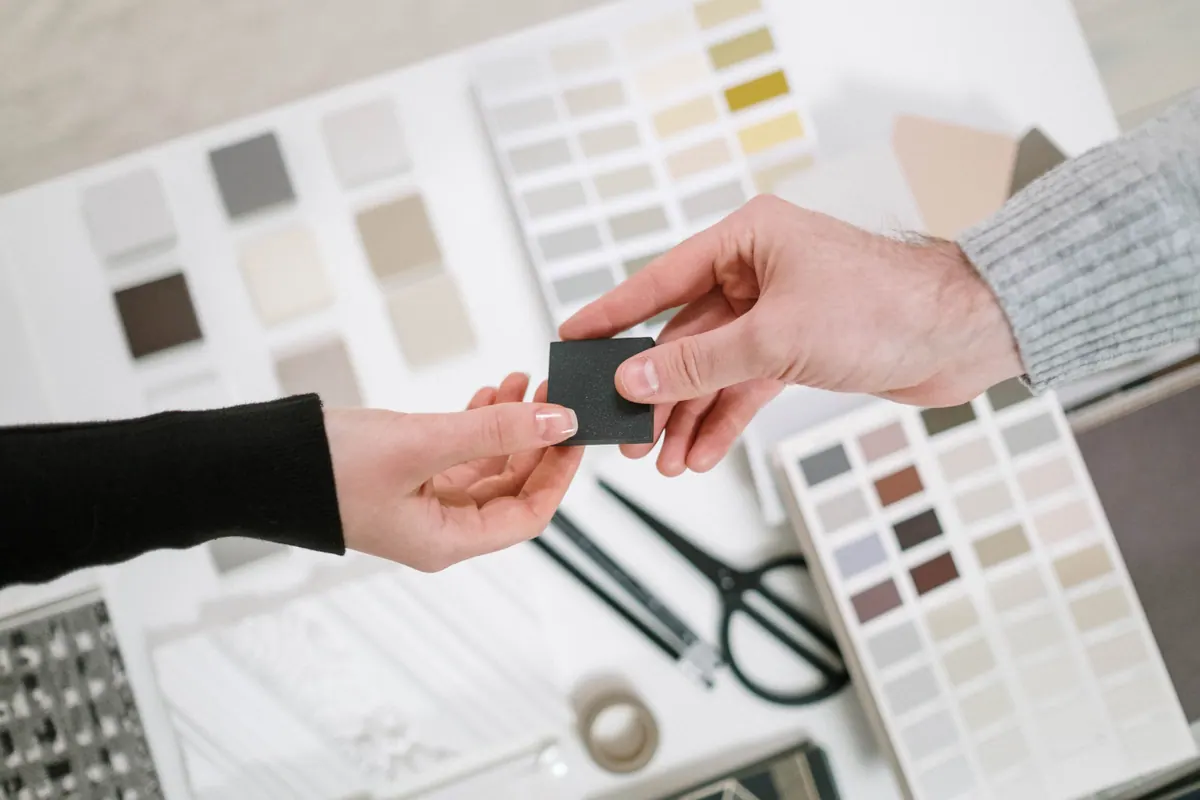 Dos personas intercambiando una muestra de material entre paletas de color