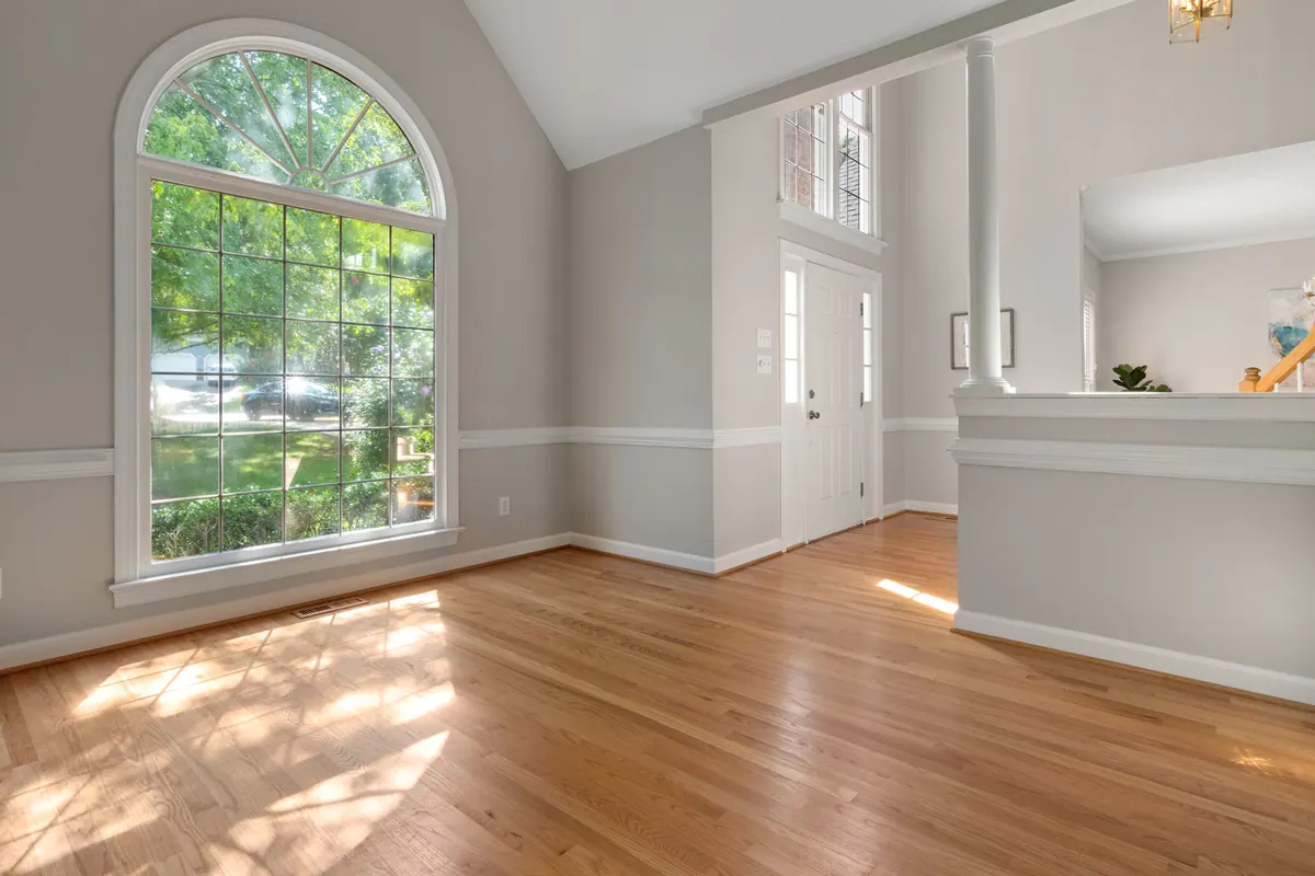 Salón vacío con una gran ventana en arco y suelo de parqué
