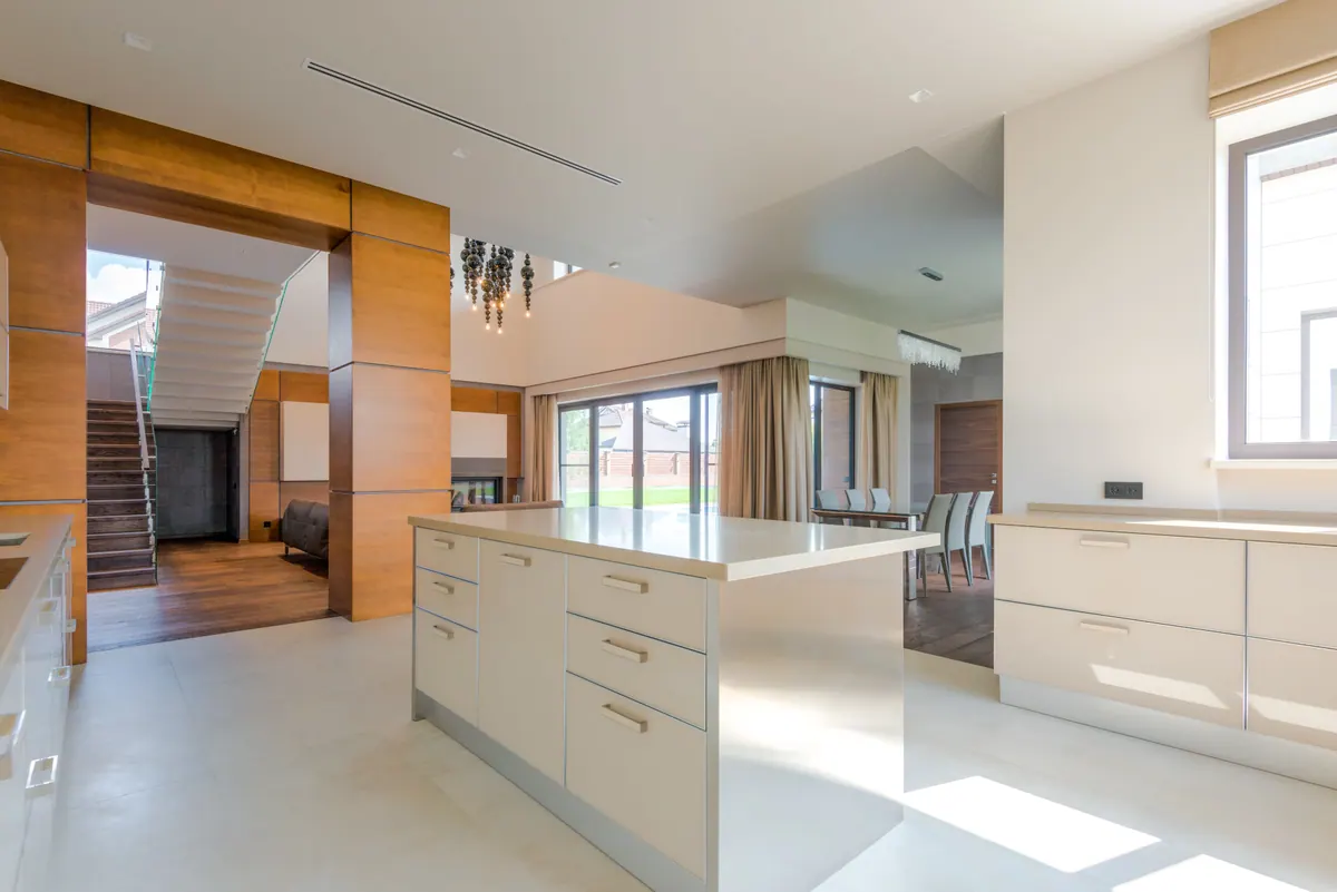 Cocina abierta con columnas de madera, isla central y escalera de vidrio al fondo