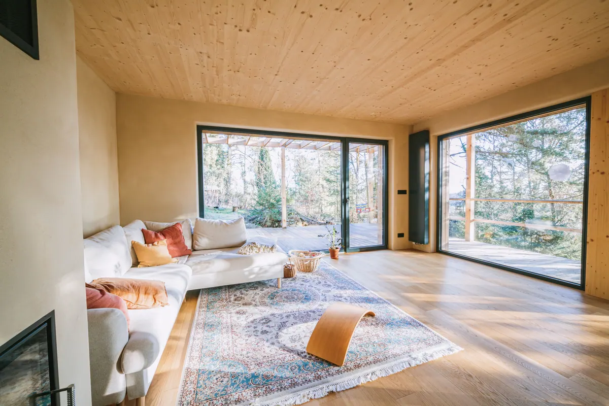 Salón con techo y suelo de madera y amplias cristaleras que dan al bosque